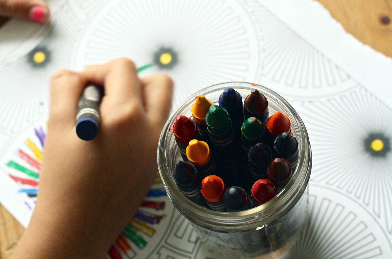 A child's hand coloring a picture with crayons, surrounded by art supplies