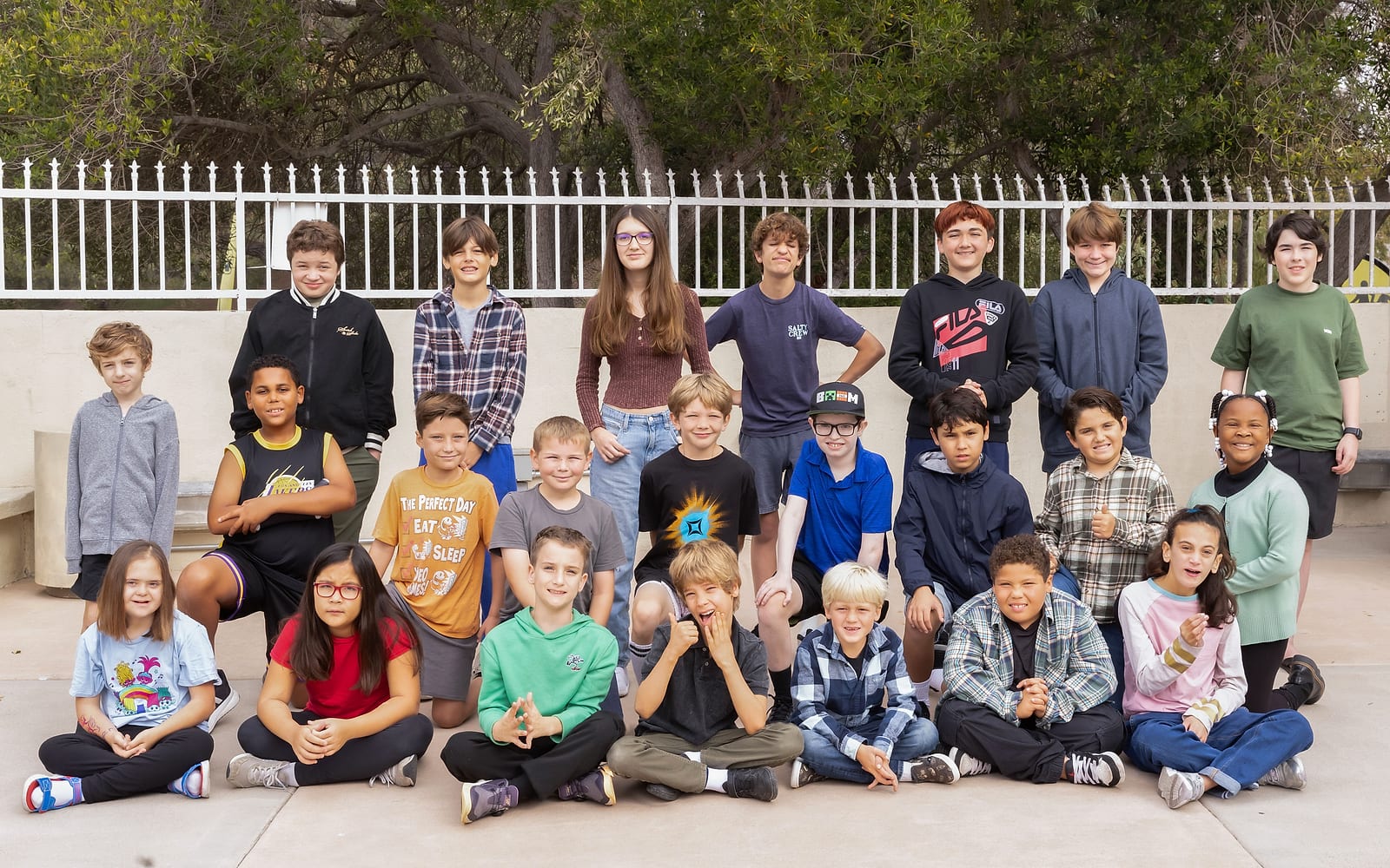 LINKS students of all ages gathered outdoors for a group photo in front of a white fence and trees