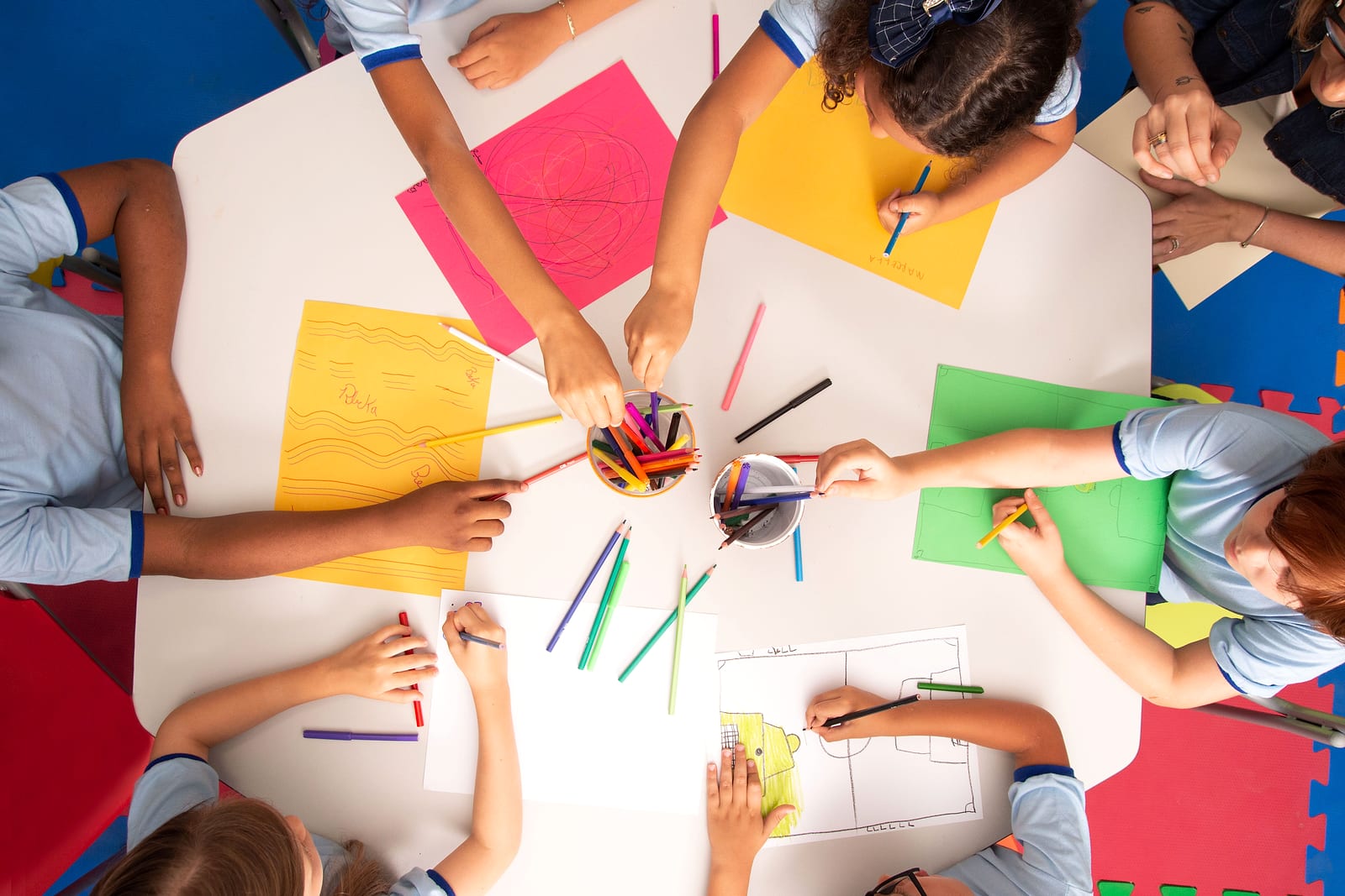 Overhead view of students in uniforms drawing on colored paper at a table