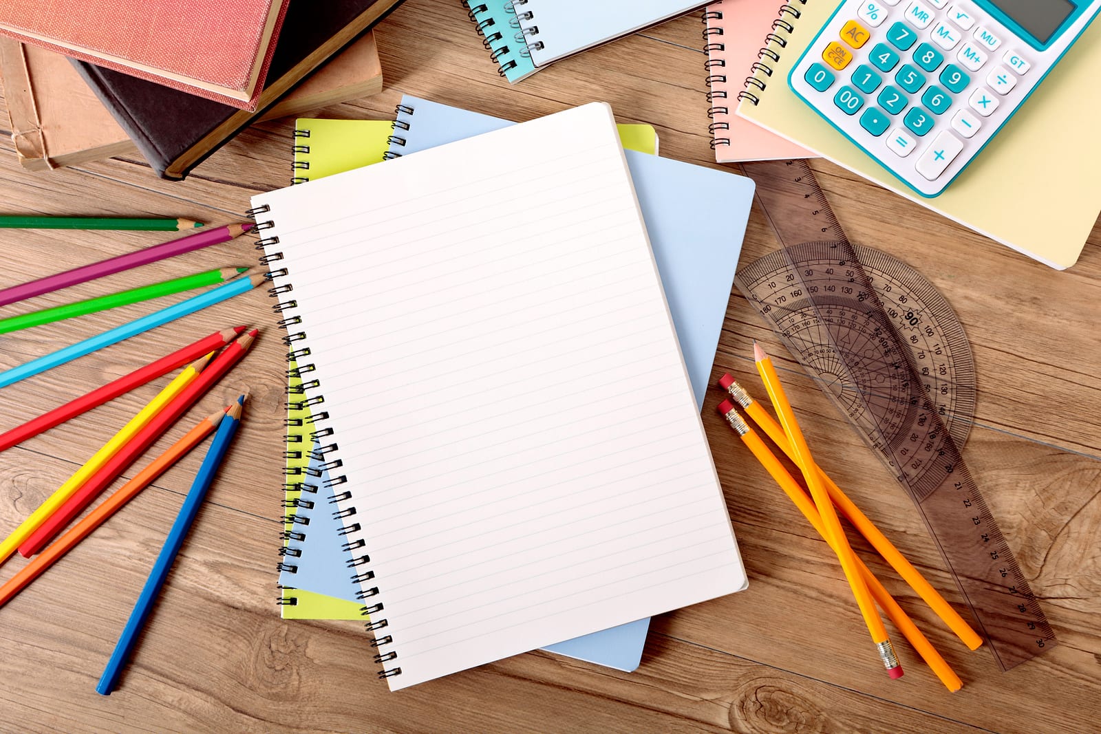 Flat lay of a blank notebook, pencils, calculator and school supplies on a wooden desk